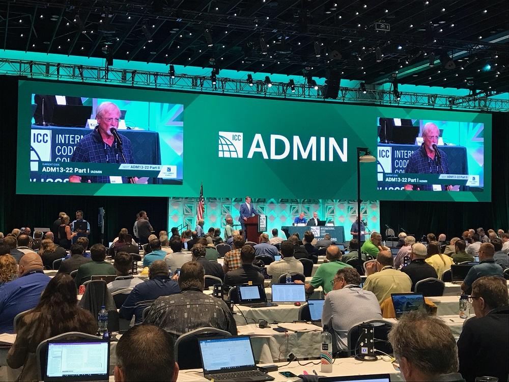 Thom Zaremba on screen in front of a large crowd at the ICC Hearings